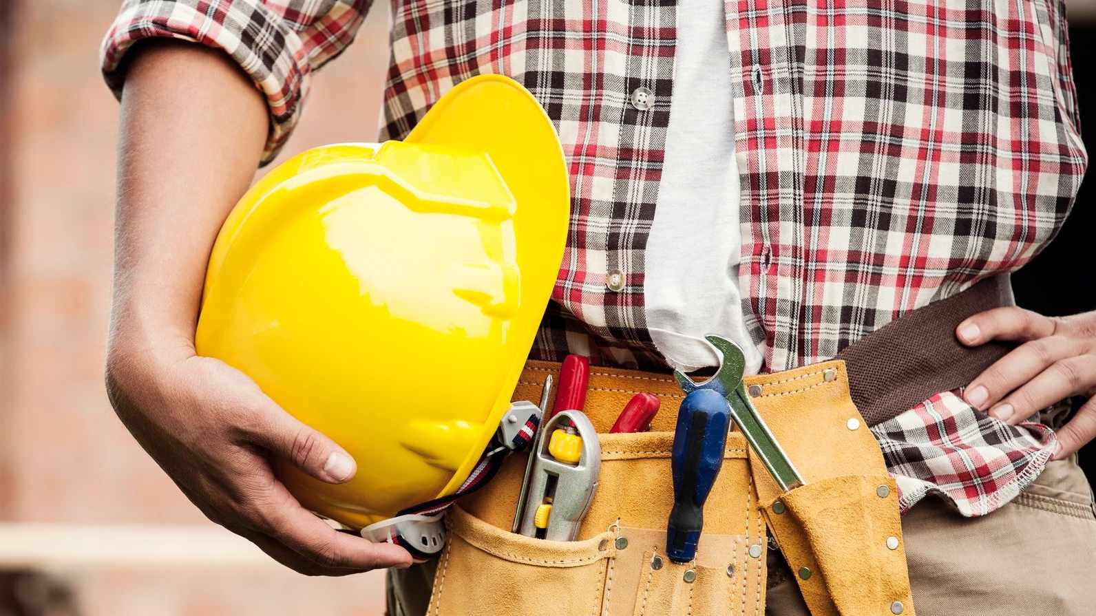Contractor with tool-belt holding a yellow hard hat.